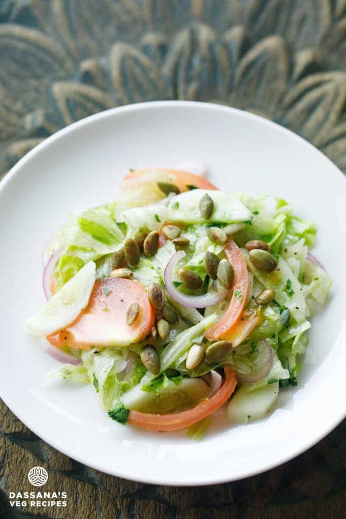 overhead shot of green salad on a white plate on a carved wooden table.