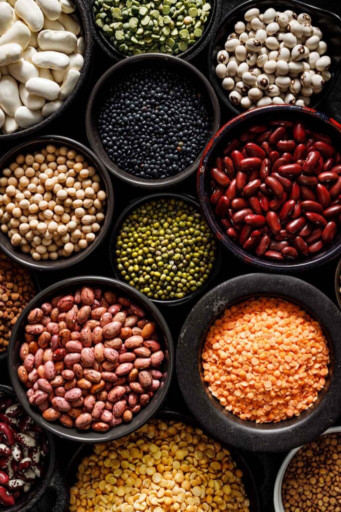 overhead shot of different types of beans, legumes and lentils filled in black bowl of various sizes.