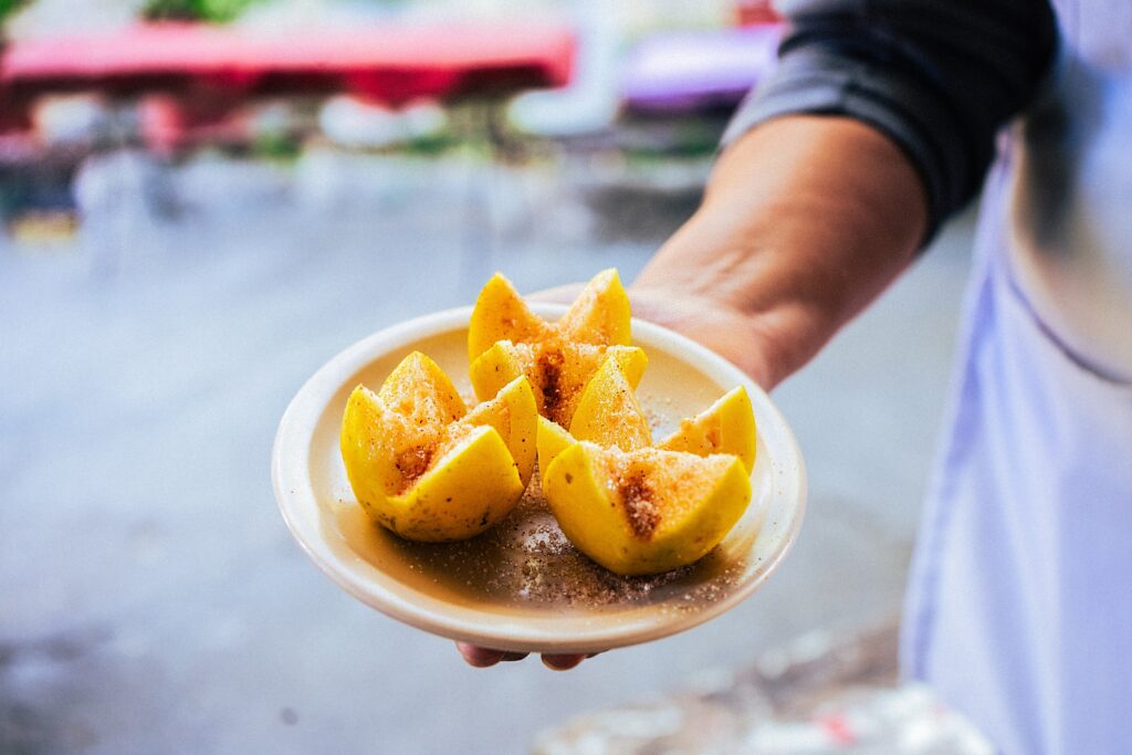 A person holds out a plate of guava slices topped with red powder.