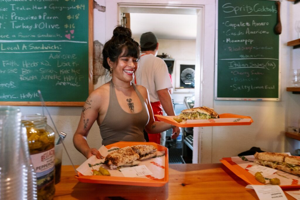 A server hands over two trays of sandwiches.