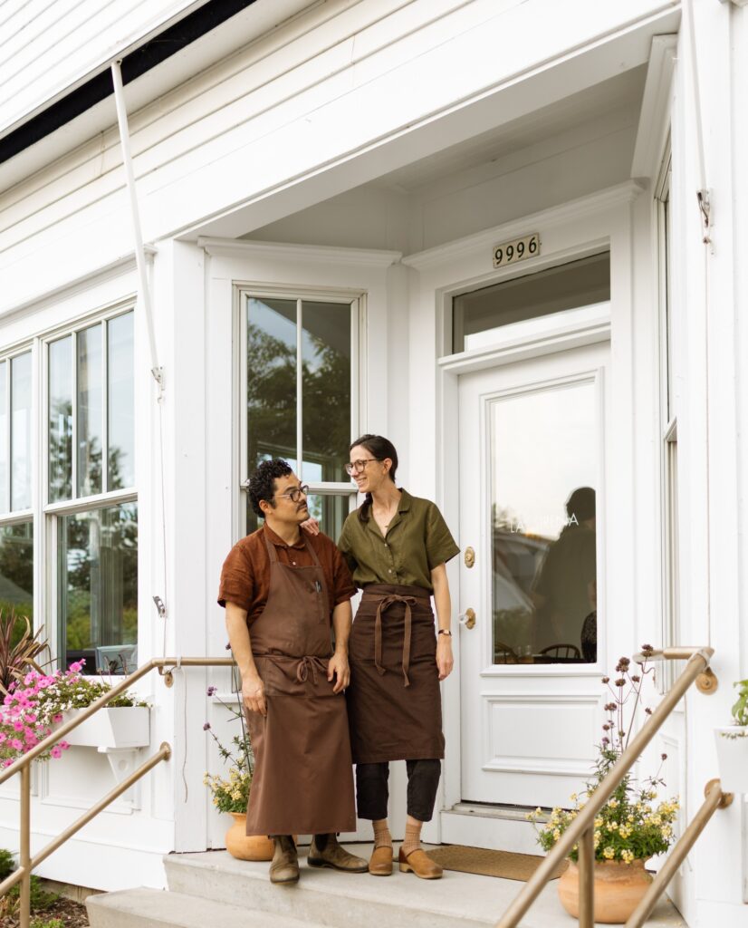 A couple stand on the doorstep of a restaurant.