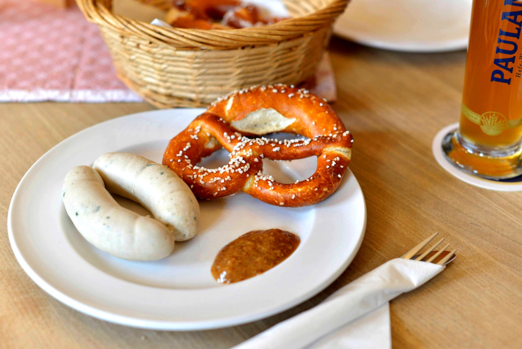A pretzel with white sausages and sauce.