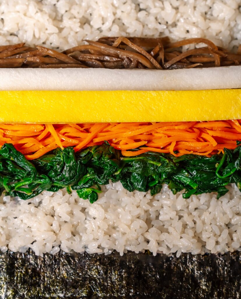 a close up image of the fillings inside a gimbap roll at tbd gimbap, with rice, burdok root, daikon, egg, carrots, spinach. each element can be seen as a layer.